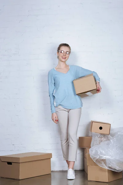 Sonriente dueño de la tienda en línea con caja de cartón mirando a la cámara en casa - foto de stock