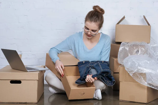 Joven empresario poner chaqueta de mezclilla en la caja de cartón, mientras que el embalaje de productos en casa oficina - foto de stock