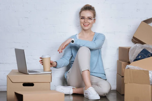 Empreendedor sorridente com café para ir sentado no chão em casa escritório — Fotografia de Stock