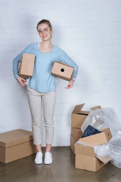 Cheerful entrepreneur holding cardboard boxes and looking at camera at home — Stock Photo