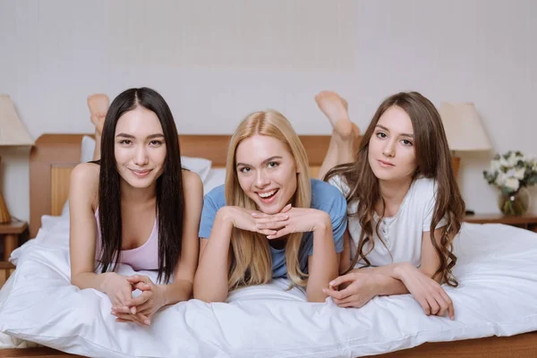 Amigos multiculturais deitado na cama e olhando para a câmera — Fotografia de Stock