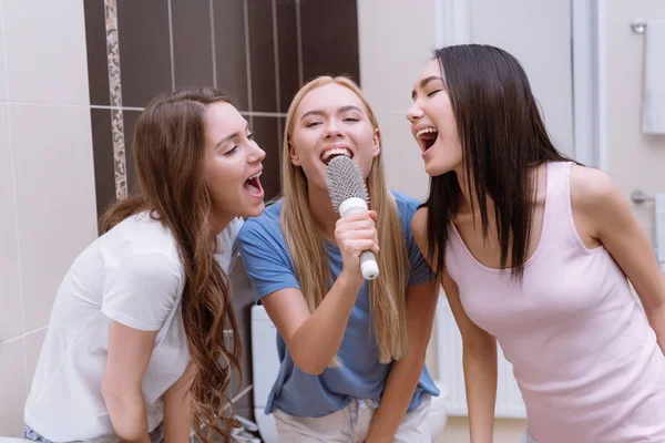 Многонациональные друзья поют в ванной комнате с круглой расческой — стоковое фото