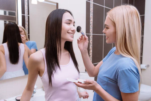 Caucasian girl applying foundation powder with makeup brush on asian friends face — Stock Photo