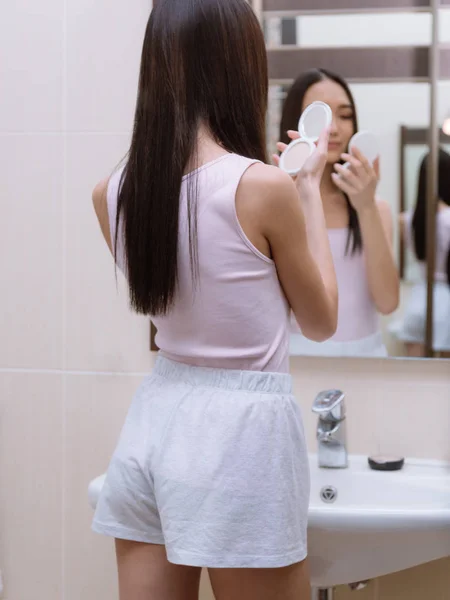 Vue arrière de asiatique fille tenant fond de teint poudre dans salle de bain — Photo de stock