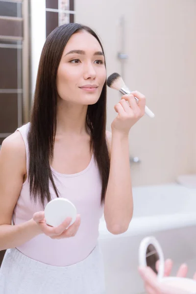 Attractive asian girl applying foundation powder with makeup brush in bathroom — Stock Photo