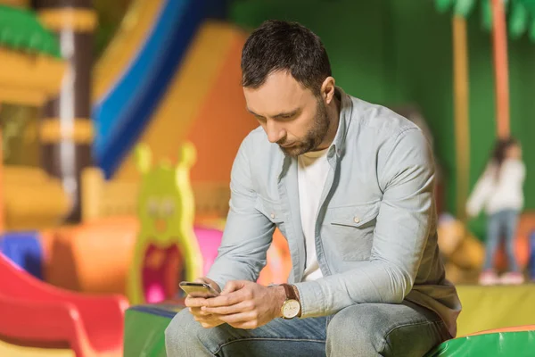 Bearded man sitting and using smartphone in entertainment center — Stock Photo
