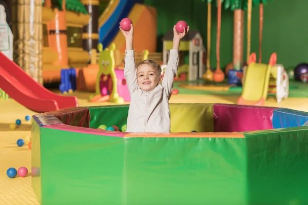 Entzückender kleiner Junge lächelt in die Kamera, während er im Pool mit bunten Kugeln spielt — Stockfoto