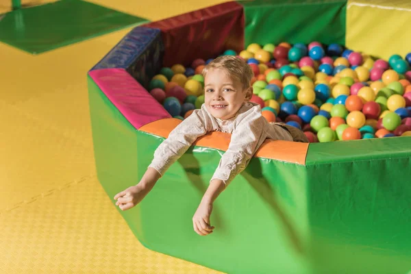 Cute little boy smiling at camera while playing in pool with colorful balls — Stock Photo