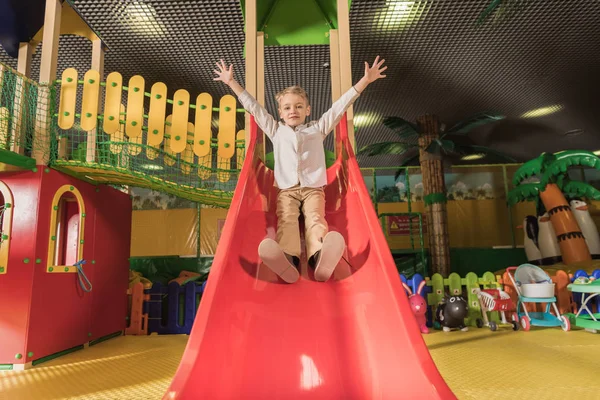 Lindo niño feliz con las manos levantadas jugando en la diapositiva en el centro de entretenimiento - foto de stock