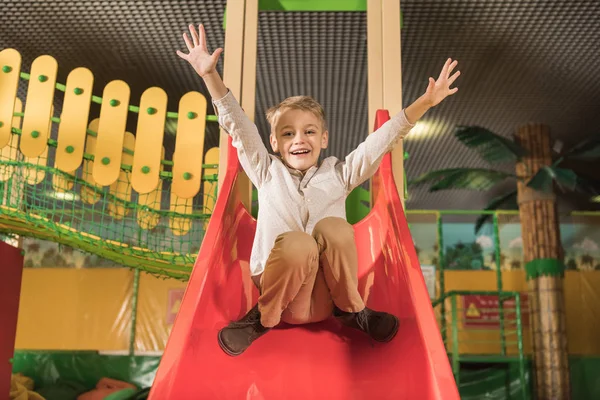 Adorable little boy smiling at camera while playing on slide in game center — Stock Photo