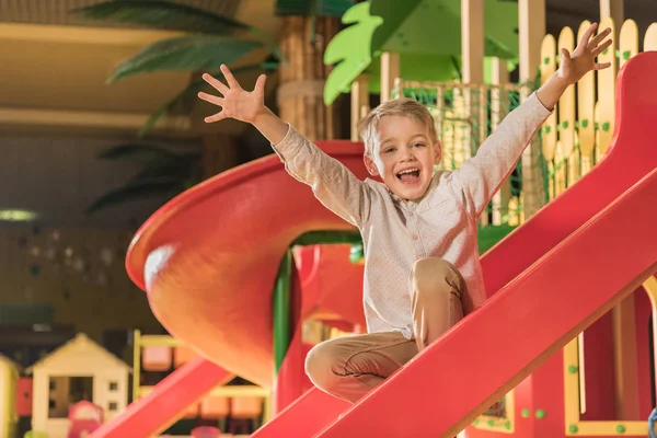 Feliz niño sonriendo a la cámara mientras juega en la diapositiva en el centro de entretenimiento - foto de stock