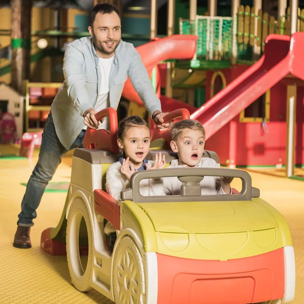 Heureux père portant des enfants sur la voiture jouet au centre de divertissement — Photo de stock