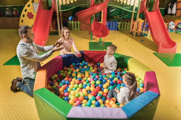 Visão de alto ângulo de família feliz com duas crianças adoráveis brincando com bolas coloridas no centro de entretenimento — Fotografia de Stock