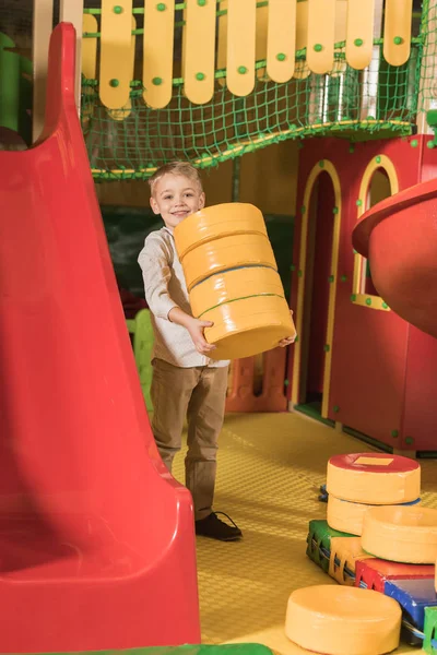 Glücklicher kleiner Junge lächelt in die Kamera, während er im Unterhaltungszentrum mit Blöcken spielt — Stockfoto
