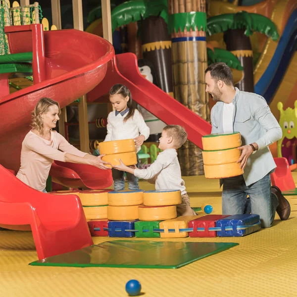 Счастливая семья с двумя маленькими детьми, играющими вместе в развлекательном центре — стоковое фото