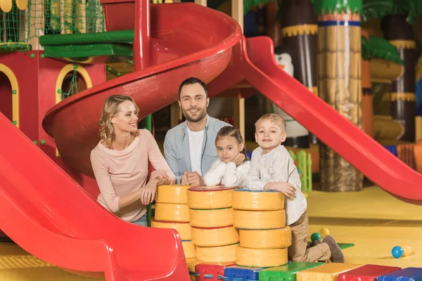 Famiglia felice con due bambini sorridenti alla macchina fotografica mentre giocano insieme nel centro di intrattenimento — Foto stock