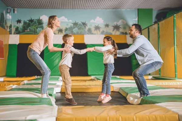 Vue latérale de la famille heureuse avec deux enfants jouant ensemble dans le centre de jeu — Photo de stock