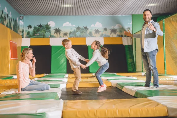Pais felizes com crianças adoráveis de mãos dadas e pulando no centro de entretenimento — Fotografia de Stock