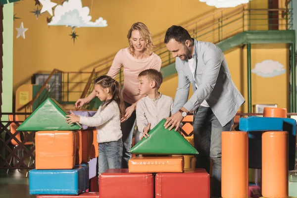 Glückliche Eltern mit entzückenden kleinen Kindern, die zusammen mit bunten Bausteinen im Spielzentrum spielen — Stockfoto