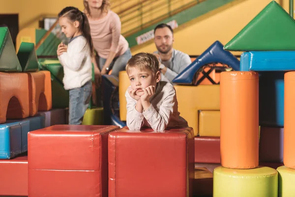 Bored little boy looking away while family playing with colorful blocks in entertainment center — Stock Photo