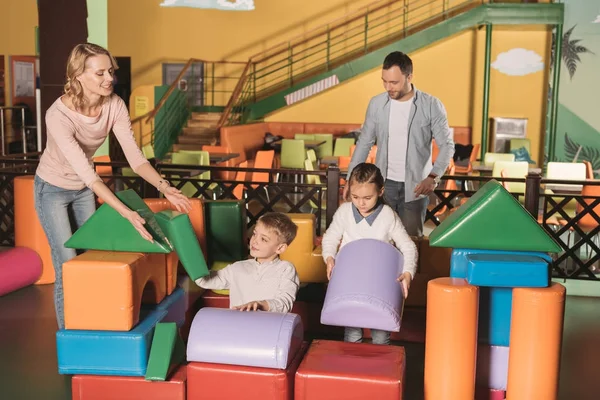 Família feliz com duas crianças brincando com blocos coloridos no centro do jogo — Fotografia de Stock