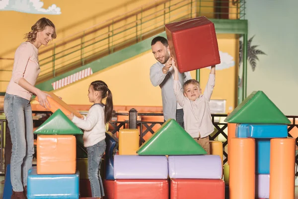 Glückliche Familie mit zwei Kindern baut Schloss mit bunten Bauklötzen im Spielzentrum — Stockfoto