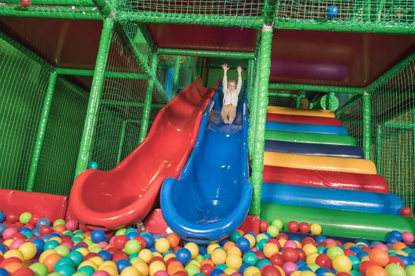 Heureux petit garçon glissant dans la piscine avec des boules colorées — Photo de stock