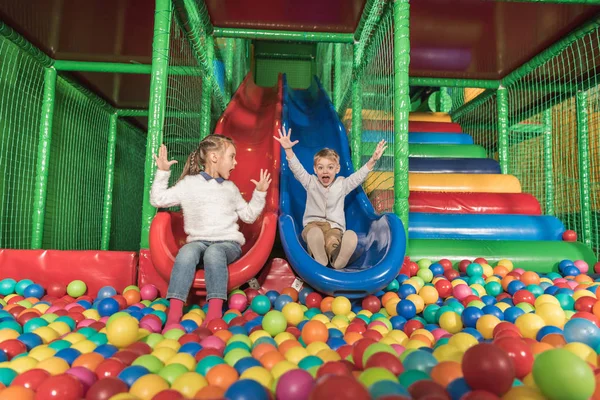Adorable heureux petits enfants glissant dans la piscine avec des boules colorées — Photo de stock