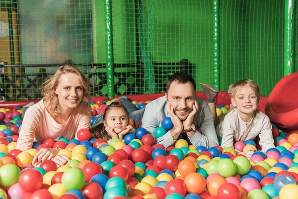 Щаслива сім'я з двома дітьми посміхається на камеру, лежачи в басейні з різнокольоровими кульками — стокове фото