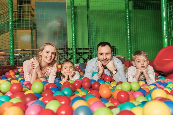 Счастливая семья улыбается в камеру, лежа в бассейне с красочными шариками — стоковое фото