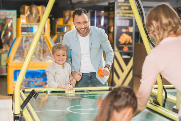 Счастливая семья с двумя детьми играть в воздушный хоккей вместе в развлекательном центре — стоковое фото