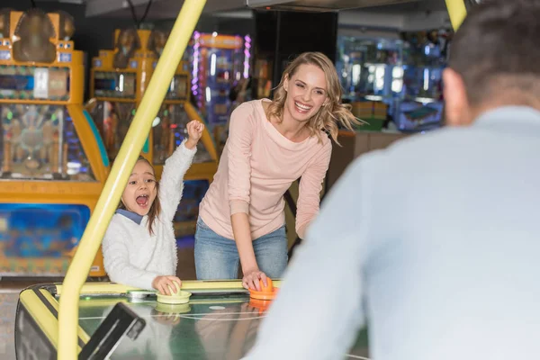 Selective focus of parents with happy little daughter playing air hockey in game center — Stock Photo
