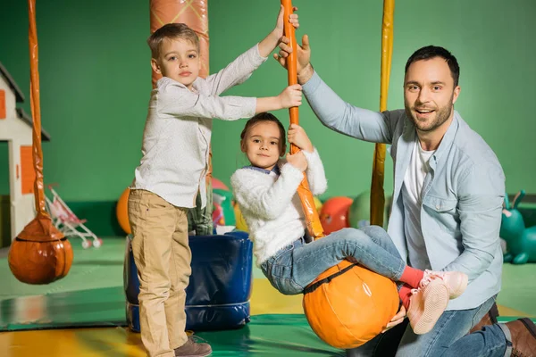 Heureux père avec adorables enfants souriant à la caméra tout en jouant dans le centre de divertissement — Photo de stock