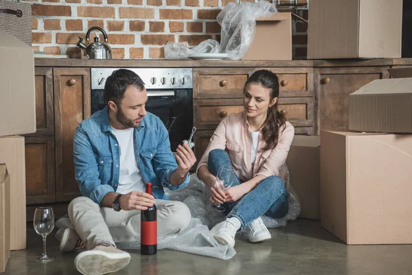 Young couple opening bottle of wine while celebrating relocation in new house — Stock Photo