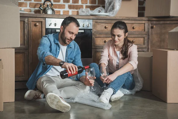 Sonriente joven pareja bebiendo vino en nueva casa — Stock Photo