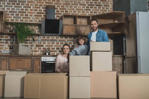 Happy family with stacks of boxes smiling at camera while moving home — Stock Photo