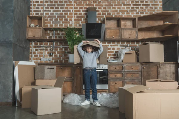 Petit garçon regardant la caméra tout en jouant avec la boîte en carton pendant la relocalisation — Photo de stock