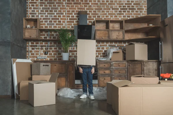 Niño pequeño de pie con caja de cartón en la cabeza mientras se muda a casa — Stock Photo