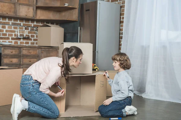 Vista lateral de la madre y el hijo dibujo en caja de cartón en nuevo apartamento - foto de stock