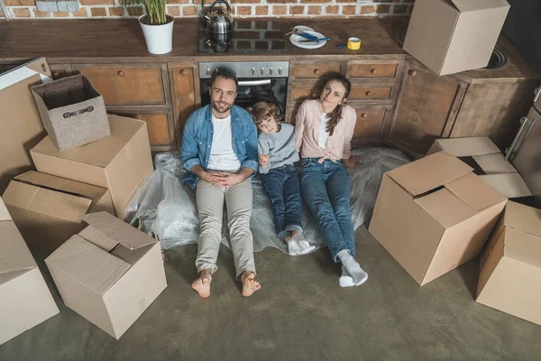 Blick aus der Vogelperspektive auf eine glückliche Familie, die während des Umzugs auf dem Boden sitzt und in die Kamera lächelt — Stockfoto