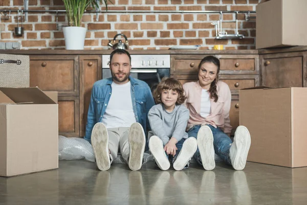 Famiglia felice con un bambino che sorride alla macchina fotografica mentre si siede sul pavimento durante il trasferimento — Foto stock