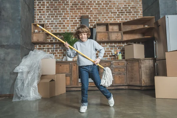 Bonito feliz menino brincando com esfregona no novo apartamento — Fotografia de Stock