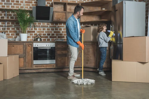 Glücklicher Vater und Sohn in Gummihandschuhen putzen neue Wohnung nach dem Umzug — Stockfoto