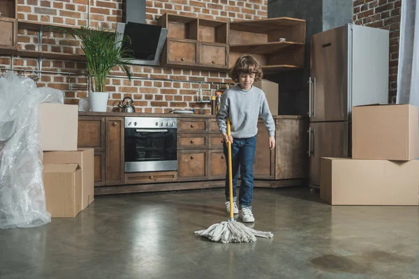 Menino bonito com esfregona limpeza nova casa após a realocação — Fotografia de Stock