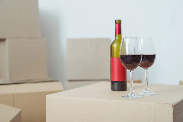 Close-up view of bottle and glasses with wine on cardboard box during relocation — Stock Photo