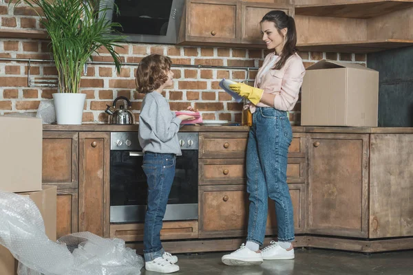 Мати з сином посміхається один одному під час миття тарілок після переїзду в новому будинку — стокове фото