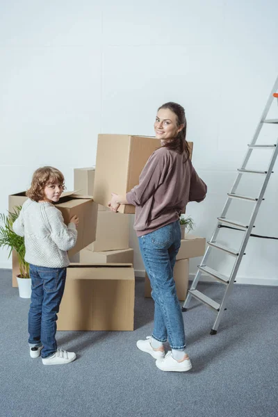 Счастливая мать и сын улыбаются перед камерой, упаковывая коробки во время переезда — стоковое фото