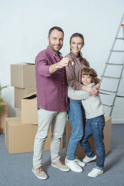 Glückliche Familie mit einem Kind, das in die Kamera lächelt und Schlüssel aus der neuen Wohnung hält — Stockfoto