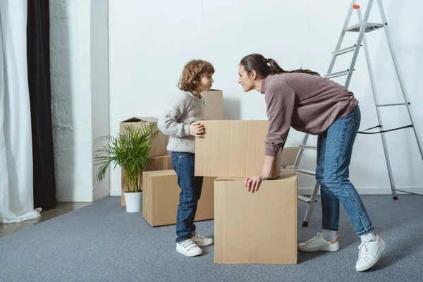 Heureux mère et fils regardant les uns les autres tout en emballant des boîtes pendant la réinstallation — Photo de stock