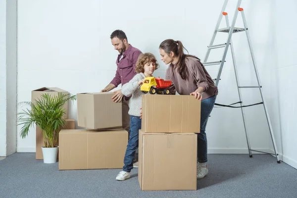 Family with one kid packing cardboard boxes while moving home — Stock Photo
